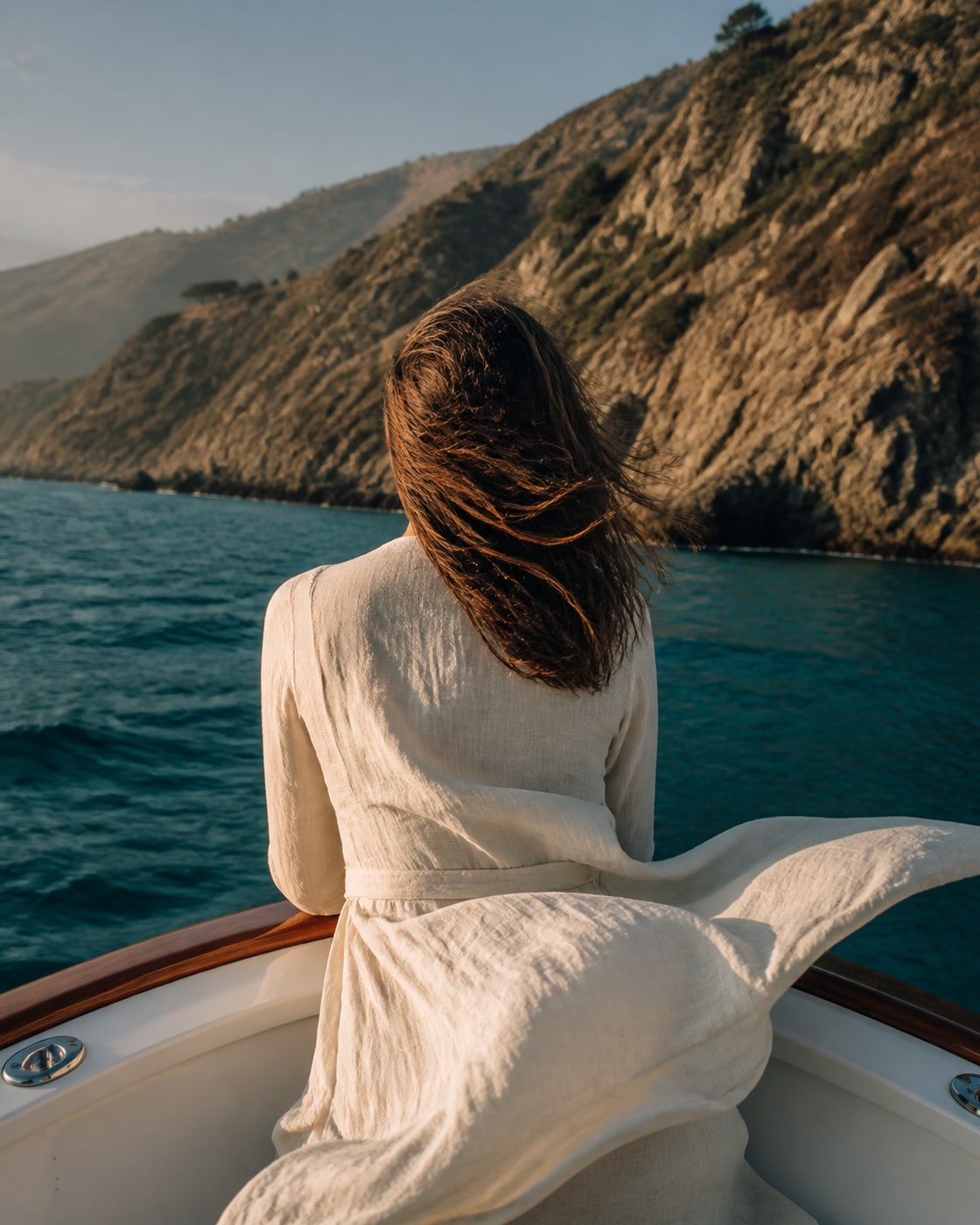 Anonymous fictional woman viewed from behind at the bow facing a rugged coastline